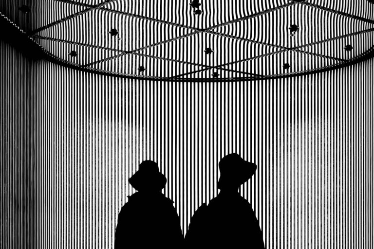 Two silhouetted figures wear hats against a striped background.